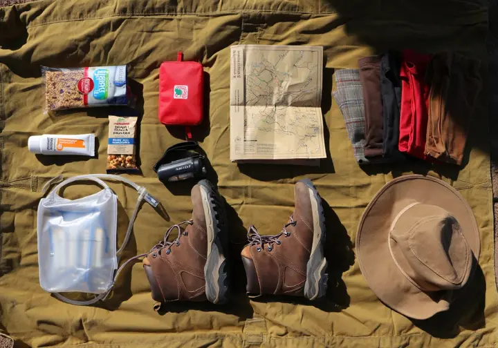A flat lay of essential hiking gear, including boots, water, snacks, and a map, representing comprehensive preparation for a Bear Mountain hike.