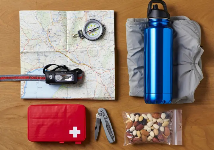 A flat lay of essential hiking gear, including a map, compass, first-aid kit, and water bottle, representing preparation for hiking.
