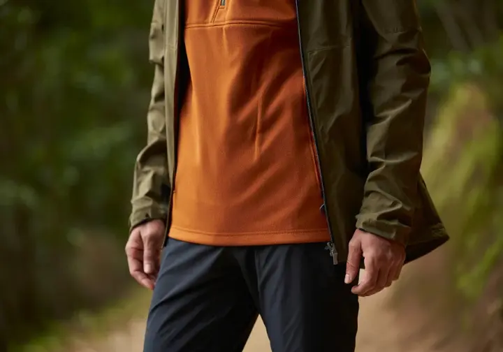 A thru-hiker demonstrates a multi-layered clothing system while on the trail, illustrating a wearable micro-environment for a thru-hiking gear list.