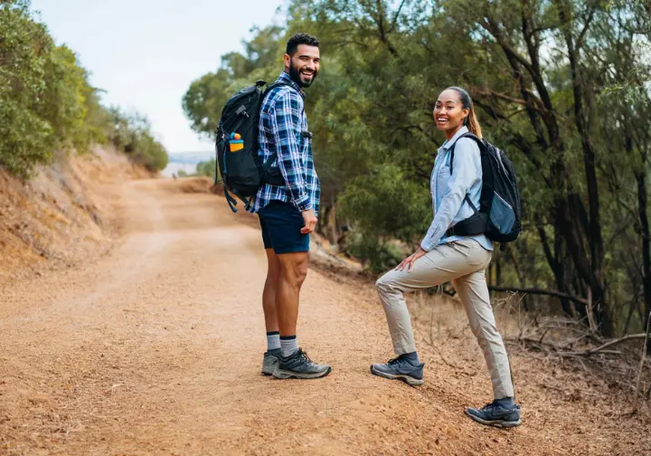 Two hikers demonstrating trail etiquette, with one yielding to the other on an uphill climb, on a well-maintained dirt trail.