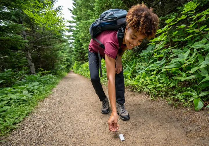 A hiker demonstrates Leave No Trace principles by picking up trash on a well-defined trail at Bear Mountain, emphasizing trail protection.