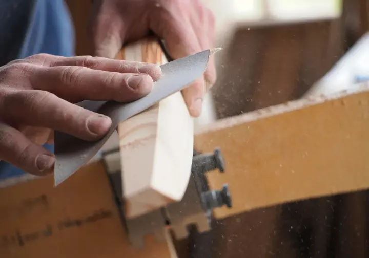Hands meticulously sand a wooden hiking stick, shaping an ergonomic grip, illustrating the transformation from branch to functional staff.
