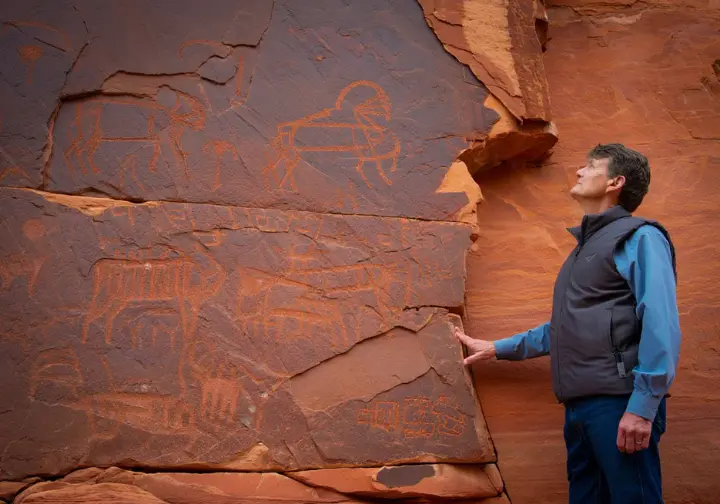A person examining ancient petroglyphs on Aztec Sandstone, symbolizing the landscape and history of Valley of Fire.