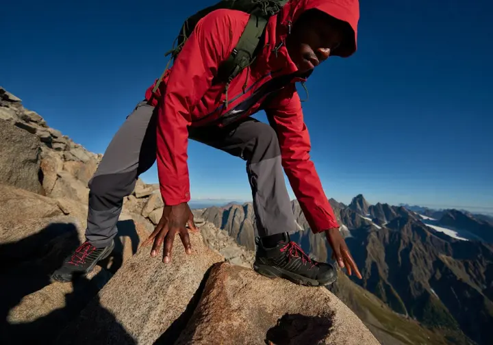 An experienced hiker navigates steep, rocky terrain on a mountain trail with dramatic panoramic views, illustrating Vancouver's best challenging hikes.