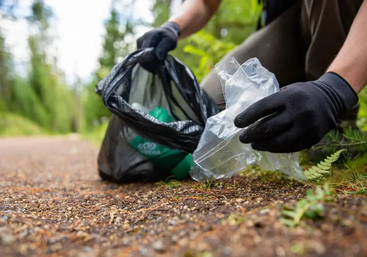 Hands of a hiker picking up litter from a trail, symbolizing environmental responsibility and the duty of care in hiking.