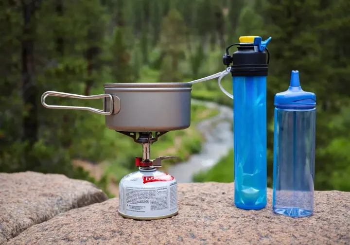 A compact backcountry kitchen setup with a stove, pot, water filter, and bottle, representing the sustenance system for a thru-hiking gear list.
