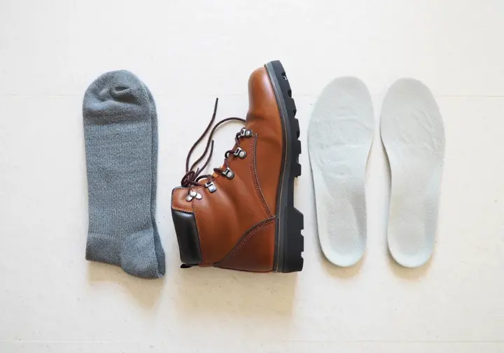 A complete hiking footwear system, including a hiking shoe, socks, and aftermarket insoles, arranged to illustrate their collective role for happy feet when choosing what shoes to wear when hiking.