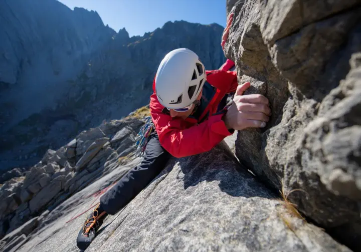 A hiker in a helmet scrambles up a steep rock face on a mountain, illustrating advanced skills for dedicated hikers.