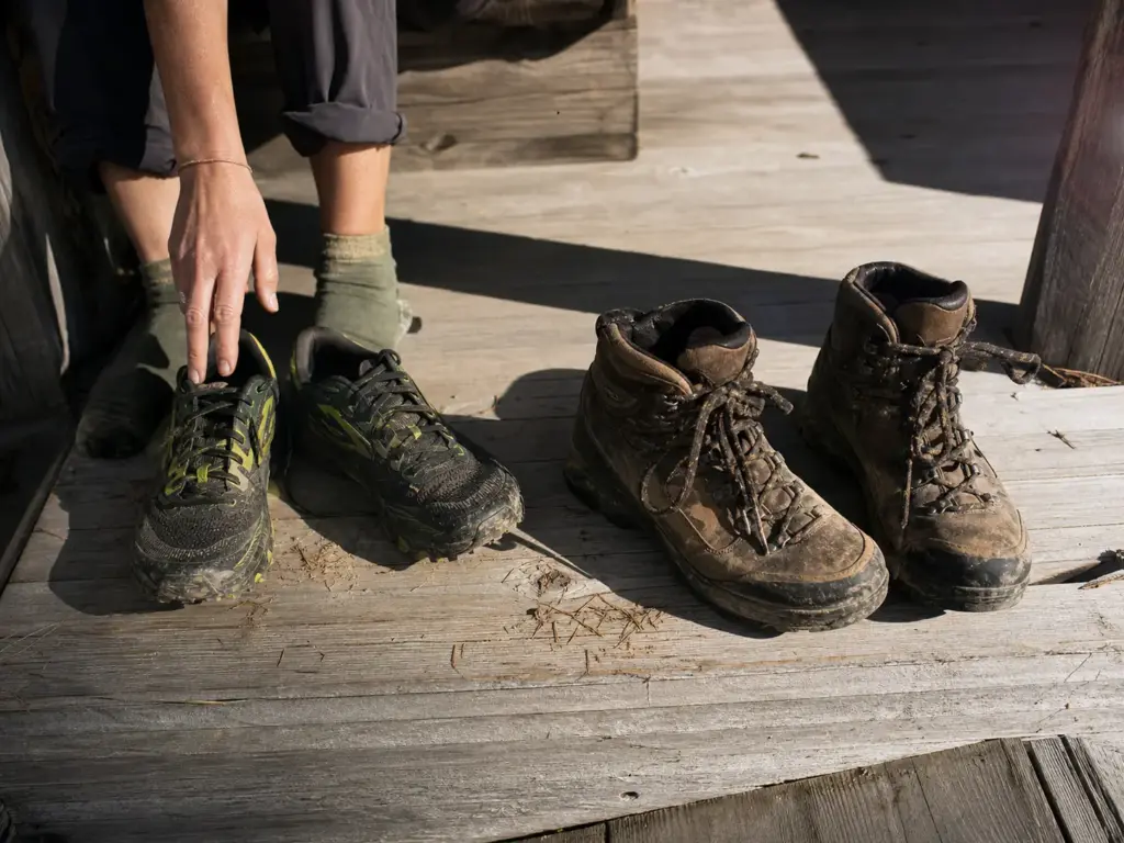 Trail running shoes and heavy leather hiking boots placed side by side on a wooden porch for comparison