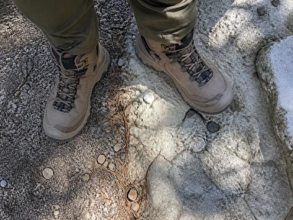 Hiking boots stepping from crushed stone onto bare conglomerate bedrock at Minnewaska