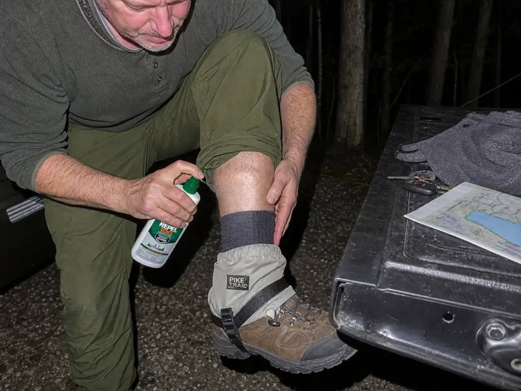 Applying DEET repellent over ankle gaiters at a Long Island trailhead before hiking in tick country.