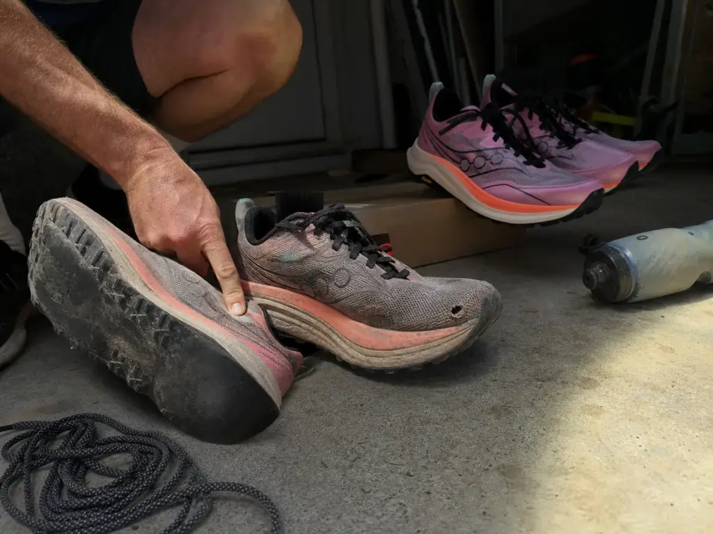 Worn out trail running shoes with flattened lugs and a hole in the mesh next to a new pair