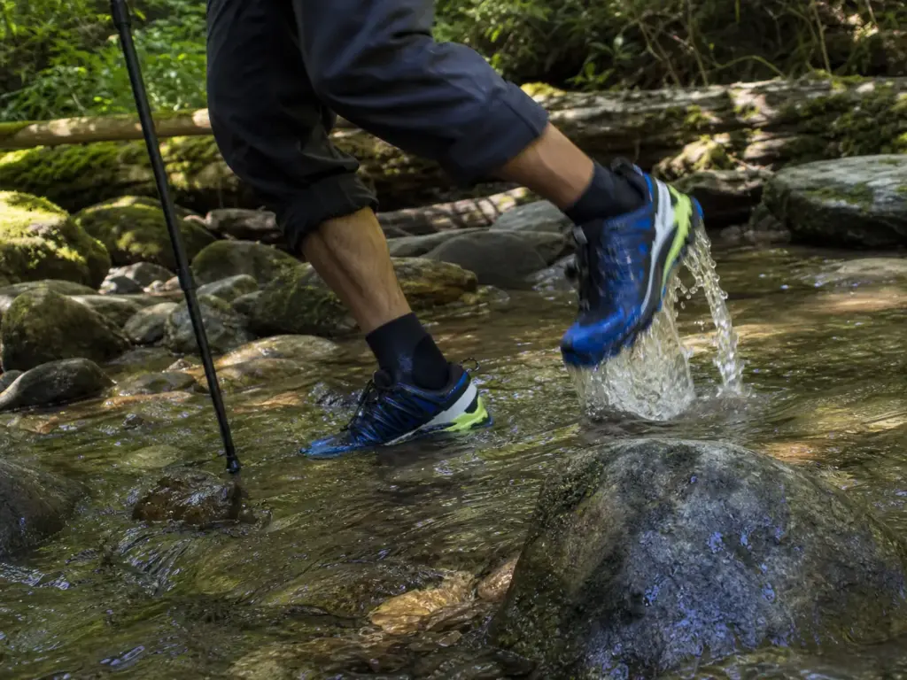 Hiker stepping through a shallow creek in trail running shoes with water draining from the mesh upper