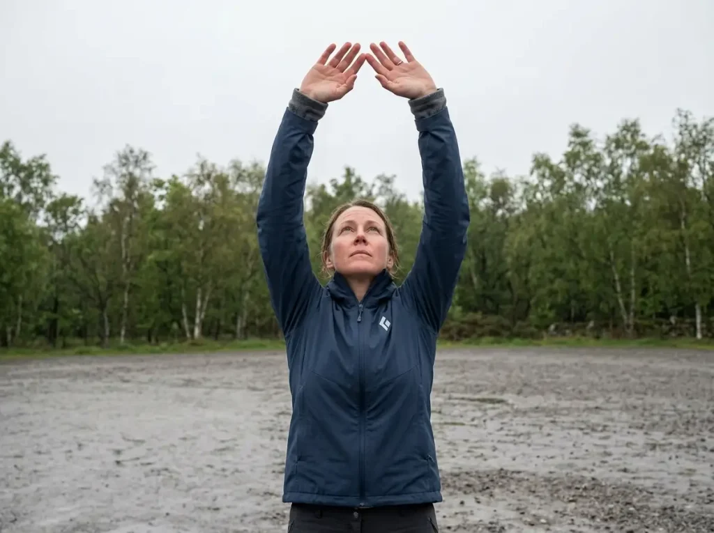 Hiker reaching both arms overhead to check rain jacket sleeve length over a fleece