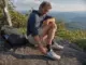 Best Thru-Hiking Shoes That Actually Reach 700 Miles Thru-hiker checking worn Altra Lone Peak trail runners on an Appalachian Trail ridgeline