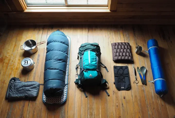 A flat lay of backpacking gear showing a progression from beginner items on the left to expert ultralight equipment on the right.