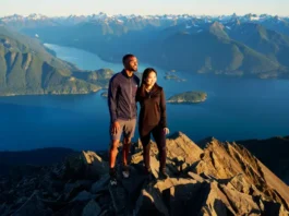 Two hikers watching the sunset from a mountain summit overlooking the epic coastal mountain scenery of Vancouver, BC.