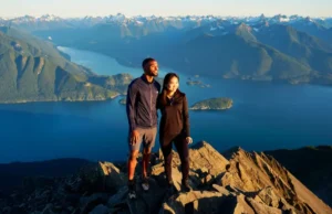 Ultimate Guide to the Best Hikes in Vancouver BC Two hikers watching the sunset from a mountain summit overlooking the epic coastal mountain scenery of Vancouver, BC.