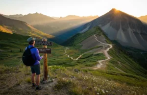 Colorado Trail Guide: Hikes Rated By Difficulty A hiker stands at a trail junction overlooking a panoramic vista of the Colorado Rockies at sunrise, with multiple trails of varying difficulty visible in the valley below.