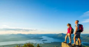 Conquer the Adirondacks: Lake George Hiking Guide Two hikers at a summit overlook, enjoying the panoramic view of Lake George and the Adirondack Mountains at sunrise.
