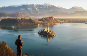 Essential Hikes in Lake Bled: From Easy Walks to Peaks A hiker at the Ojstrica viewpoint looking at the iconic panoramic view of Lake Bled, Slovenia at sunrise, with the island and castle visible.