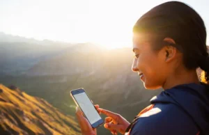 Free Hiking Apps Ranked: From Trail Discovery to Safety A hiker stands confidently on a mountain summit at golden hour, looking out at a stunning valley while checking a trail map on her smartphone.