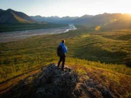 A backpacker overlooks a vast, trailless valley and the Brooks Range mountains while backpacking in Gates of the Arctic National Park.