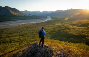 Backpacking Gates of the Arctic: Routes & Planning Guide A backpacker overlooks a vast, trailless valley and the Brooks Range mountains while backpacking in Gates of the Arctic National Park.