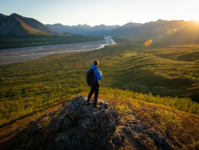 A backpacker overlooks a vast, trailless valley and the Brooks Range mountains while backpacking in Gates of the Arctic National Park.