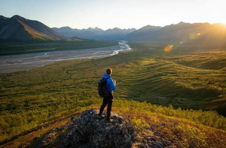 A backpacker overlooks a vast, trailless valley and the Brooks Range mountains while backpacking in Gates of the Arctic National Park.