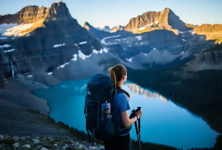 A backpacker stands on a high mountain pass in Glacier National Park at sunrise, looking out over glacial lakes and peaks, prepared for a multi-day trip.