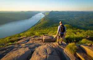 Major Welch Trail Bear Mountain: An Expert Field Guide A hiker on a rock scramble on the Major Welch Trail, looking at the panoramic view of the Hudson River from Bear Mountain at sunset.