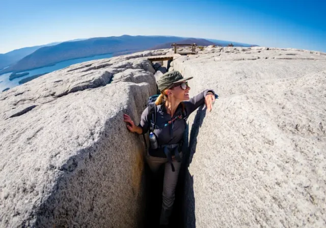 A hiker emerges from the narrow Lemon Squeeze rock scramble at Mohonk Preserve, looking out at the panoramic view of the Hudson Valley from the clifftop.