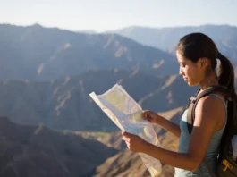 A hiker stands at a Southern California mountain overlook at sunrise, thoughtfully studying a map to plan her route for a skill-building hike.