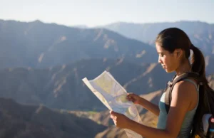 Best Hiking Trails in Southern California: A Skill Guide A hiker stands at a Southern California mountain overlook at sunrise, thoughtfully studying a map to plan her route for a skill-building hike.