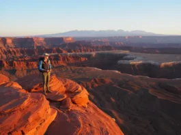 A hiker gazes out at a sweeping sunrise vista of canyons and mountains from a red rock overlook near St. George, Utah.