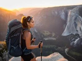 A skilled female hiker with a backpack looks out over a spectacular mountain valley at sunrise, representing the rewarding challenge of USA bucket list hikes.