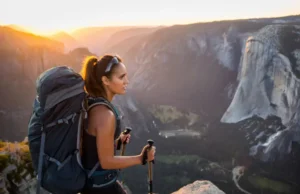 USA Bucket List Hikes: Ranked by Skill & Prep Needed A skilled female hiker with a backpack looks out over a spectacular mountain valley at sunrise, representing the rewarding challenge of USA bucket list hikes.