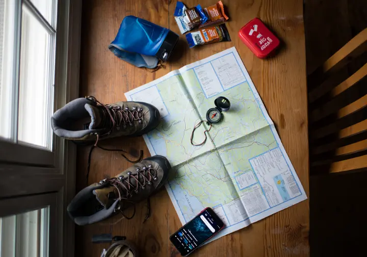 Essential hiking gear for Breakneck Ridge, including a trail map, compass, boots, and water, laid out for mission planning and preparation.