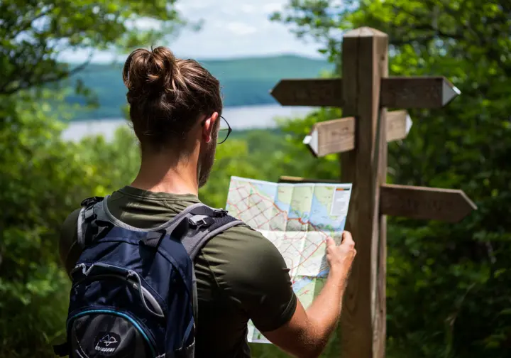 A hiker studies a map at a trail junction with multiple signs, representing the choice of alternatives to the Breakneck Ridge hike.