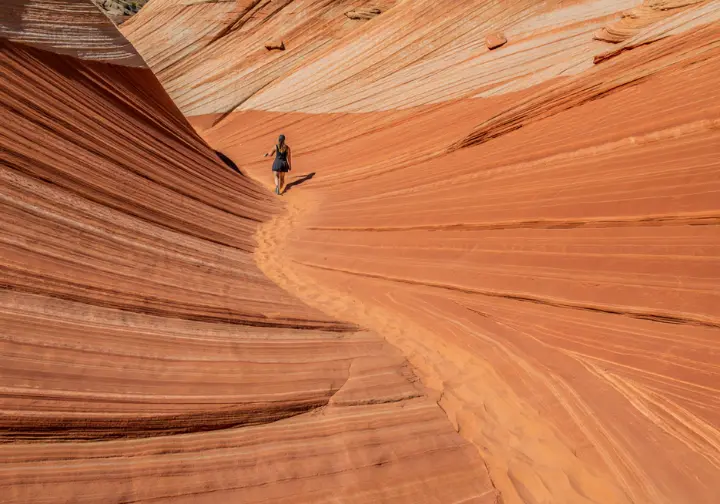 A hiker follows a sandy trail as it winds through the massive orange and white sandstone formations of Snow Canyon State Park, Utah