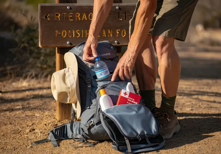 A prepared hiker checks their daypack with water, a sun hat, and a first aid kit at a trailhead, demonstrating the core knowledge SoCal hikers must master.