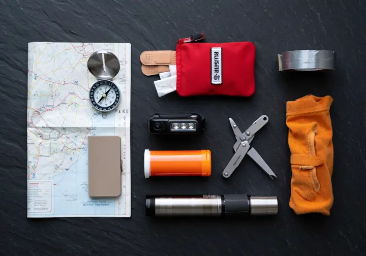 The Ten Essentials for hiking safety are arranged as systems in a neat flat lay on a dark slate surface.