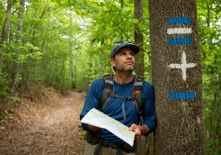 A hiker consults a map at a trail junction in Turkey Mountain Nature Preserve, with blue and white trail blazes visible on a tree.