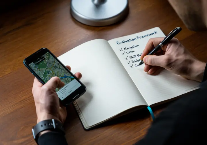A close-up of hands evaluating a hiking app on a smartphone against a detailed, five-pillar framework written in a notebook.