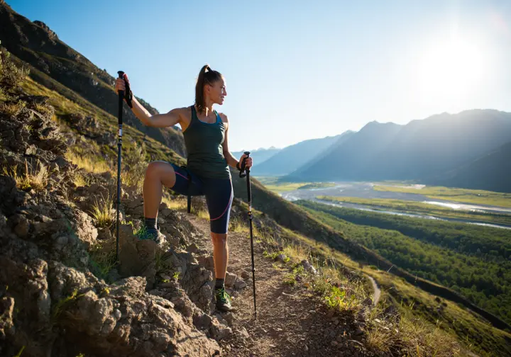 A hiker takes a rewarding break on a rocky, moderate trail in Colorado, looking back at the stunning mountain valley view she has earned.