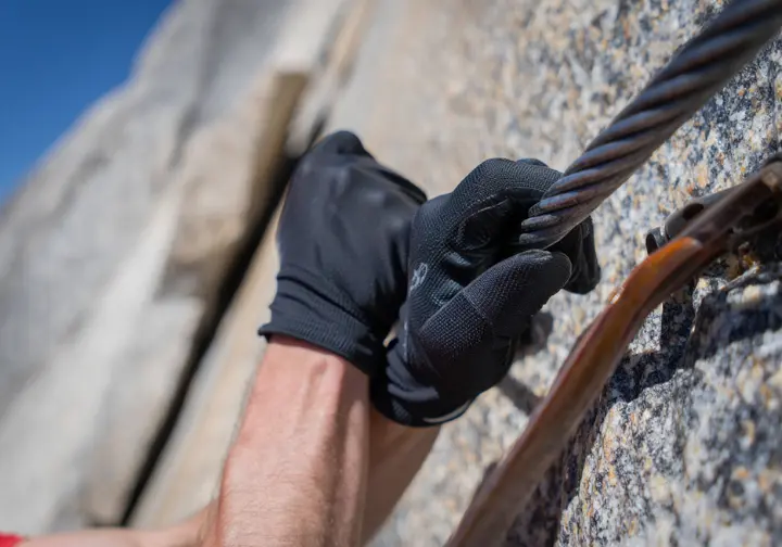 A close-up of a hiker's gloved hands gripping the steel cables on Half Dome, showing the specific preparation needed for a strenuous trek.