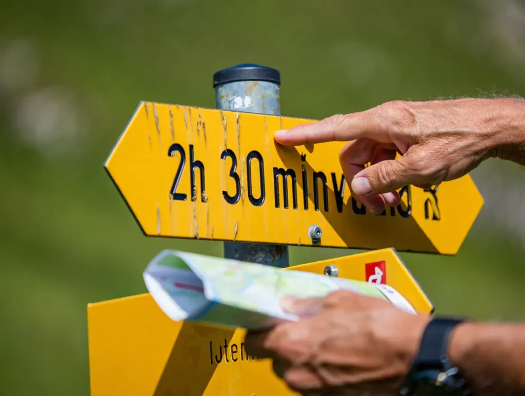A hiker's hands pointing to a yellow Swiss trail sign, demonstrating the masterclass skill of how to hike like a local.