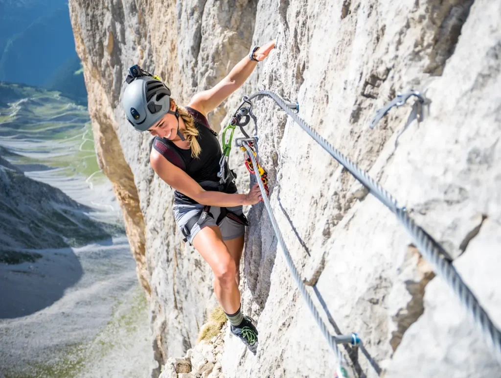 A female hiker with a helmet and harness safely navigates a challenging via ferrata section on the Slovenian Mountain Trail.