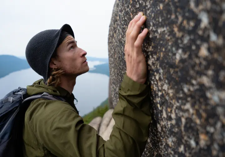 A hiker thoughtfully touches an ancient rock formation on Breakneck Ridge, connecting with the deep geology and history of the Hudson Highlands.